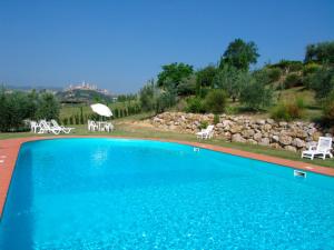 a large blue swimming pool with white chairs and umbrellas at Casale Esclusivo con Piscina e Vista su San Gimignano in San Gimignano