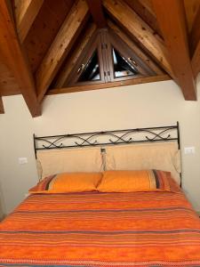 a bedroom with a bed with an orange comforter and two windows at Il Piccolo Sogno in Temù