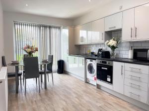 a kitchen with white cabinets and a table with chairs at Wembley Stadium, Modern&Cozy Apartment with Garden in London