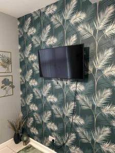 a flat screen tv hanging on a wall with a tropical wallpaper at Cozy Downtown Studio Flat in Sheffield in Sheffield
