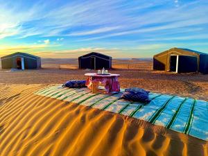 une table au milieu d'un désert avec des tentes dans l'établissement Mhamid Sahara Camp - Mhamid El Ghizlane, à M'Hamid El Ghizlane