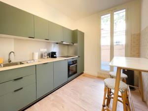 een keuken met groene kasten en een tafel met krukken bij Maison abba trois pièces in Saint-Antoine