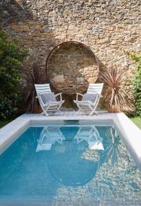 2 sedie e una piscina accanto a un muro di pietra di Llimona Suites - Adults Only a Corçà
