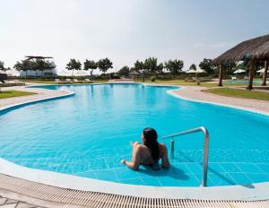 a woman sitting on the edge of a swimming pool at Luhana Chincha® Hermosa Casa de Playa in Casa Blanca