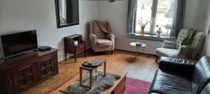 a living room with a television and a couch and chairs at Anno 1877 appartement met tuin in Slenaken