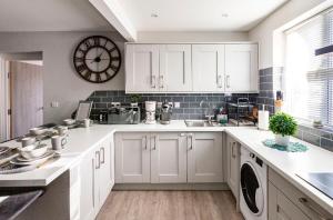 a kitchen with white cabinets and a clock on the wall at Luxury house with 4 ensuite bedrooms, free parking Wifi in Oxford