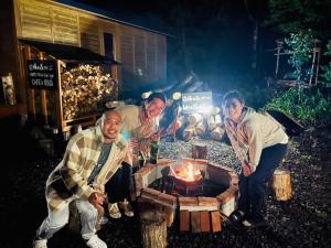 un grupo de tres hombres sentados alrededor de una hoguera en Shirakaba no mori Cottage - Vacation STAY 01176v, en Abashiri