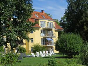 uma casa amarela com cadeiras brancas no quintal em Holiday apartment Seagull em Bad Saarow