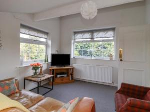 a living room with a couch and a tv and two windows at Foxholes Lodge in Settle