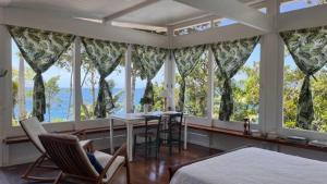 a bedroom with large windows and a table and chairs at BH58: Refúgio Romântico com Vista pro Mar in Ubatuba