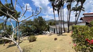 a yard with palm trees and a house and the ocean at BH58: Refúgio Romântico com Vista pro Mar in Ubatuba