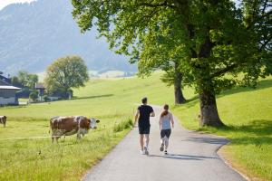 a man and woman walking down a road with a cow at Das Walchsee Resort in Walchsee