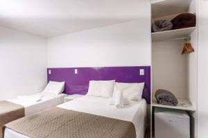 two beds in a small room with a purple wall at Zuza Slim Suítes in Maceió