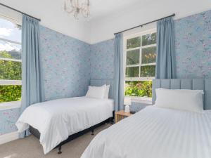 2 camas en un dormitorio con paredes y ventanas azules en Crabapple Cottage - Coromandel Town Holiday Home, en Coromandel