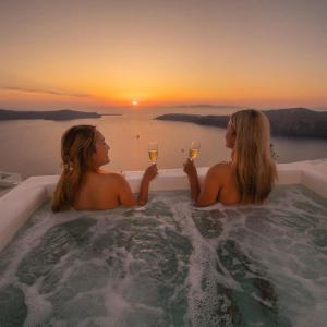 Dos mujeres sentadas en una bañera con copas de vino en Esmi Suites Santorini en Imerovigli