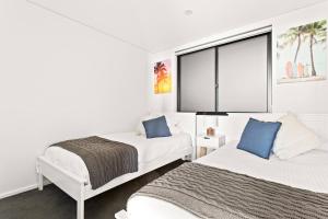 a white bedroom with two beds and a window at Ocean Views, Deck and Parking at Beach Apartment in Collaroy