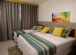 two beds in a hotel room with yellow and green pillows at Flat encantador com piscinas aquecidas, academia e playground in Olímpia