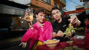 deux personnes debout autour d'une table et mangeant de la nourriture avec une boisson dans l'établissement Wink Hotel Danang Riverside - 24hrs Stay & Rooftop with Sunset View, à Đà Nẵng