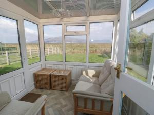 a screened in porch with a couch and chairs and windows at Hafod-y-Gors in Fairbourne