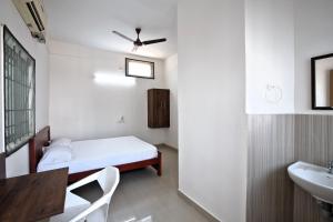 a small white room with a bed and a sink at Sarvam Lodge in Pīlamedu