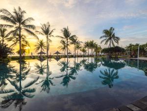 a pool with palm trees and the sunset in the background at Ayodya Resort Bali in Nusa Dua