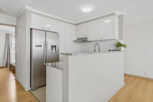cocina con armarios blancos y nevera de acero inoxidable en 2-Bed Unit with Balcony BBQ & Stunning Lake Views, en Belconnen