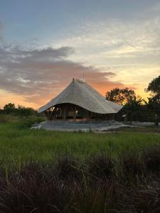 una cabaña en un campo con una puesta de sol en el fondo en Maringi Sumba by Sumba Hospitality Foundation, en Waikelo
