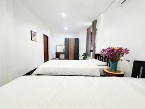 a white bedroom with two beds and a vase of flowers at An‘s Home in Chiang Mai