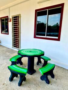 Suhana LongHouse HomeStay Sipitang في Sipitang: طاولة خضراء و كرسيين امام مبنى