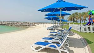 eine Reihe von Stühlen und Sonnenschirmen am Strand in der Unterkunft Blue Collection Holiday Homes - Pacific Al Marjan Island in Ras al Khaimah