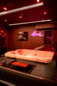 - une baignoire dans une chambre avec un panneau de néon dans l'établissement L’alcôve de la tentation, à Villeurbanne