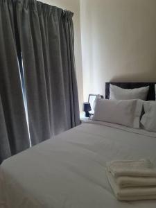 a bed with white sheets and pillows next to a window at Cozy Apartment Jhb South in Johannesburg