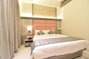 a bedroom with a large bed with a pink headboard at La Dhalia By Glitz Hotels in Thane