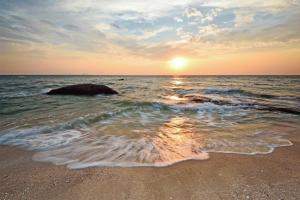 a sunset over the ocean with a rock in the water at RungRoj Panich Hotel in Ban Bang Saen (1)