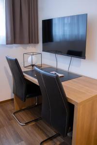 een tafel met stoelen en een televisie aan de muur bij Orange Hotel und Apartments in Neu Ulm