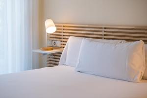 Cama blanca con almohadas blancas y lámpara en MAREA ApartHotel en Vilanova i la Geltrú
