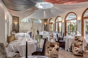 un comedor con mesas y sillas blancas y ventanas en Augustus Hotel & Resort, en Forte dei Marmi