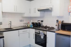 La cuisine est équipée de placards blancs et d'un four avec plaques de cuisson. dans l'établissement Spacious Grade II Listed Flint Cottage Sleeps 2, à Norwich