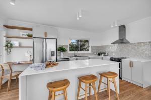 a kitchen with white countertops and wooden stools at A Short time in Merimbula