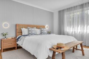 a white bedroom with a large bed and a bench at A Short time in Merimbula