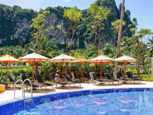 una piscina con sillas y sombrillas junto a una montaña en ibis Styles Krabi Ao Nang, en Ao Nang Beach