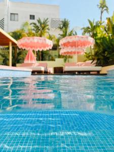 uma piscina com dois guarda-sóis e cadeiras cor-de-rosa em Tropicana Ibiza Suites - Adults Only em Playa d'en Bossa