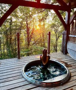 une femme assise dans un bain à remous sur une terrasse dans l'établissement Cabanes du Hérisson, cabanes perchées de standing avec spa, à Bonlieu