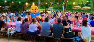 a crowd of people sitting at tables with a person in a chicken balloon at Camping Paradis Aubeterre in Aubeterre-sur-Dronne