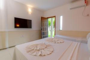 a white bedroom with two beds and a flat screen tv at Miola Hotel in Porto Seguro