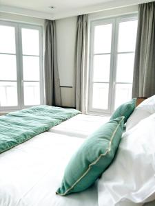 a bed with green pillows on it in a room with windows at Hôtel De La Marine in Arromanches-les-Bains