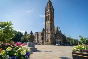 una torre de reloj frente a un edificio con flores en Rochdale Train STN, Large House, en Rochdale