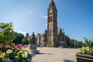 a clock tower in front of a building with flowers at Rochdale Train STN, Large House in Rochdale