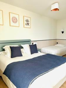 a bedroom with two beds with blue and white pillows at Hôtel De La Marine in Arromanches-les-Bains