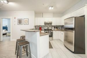 cocina con armarios blancos y nevera de acero inoxidable en New Cozy 2 Bedrooms Condo w Parking en Calgary
